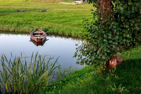 A small wooden rowing boat with a broken bottom on a calm lake near the shore. Belarusの写真素材