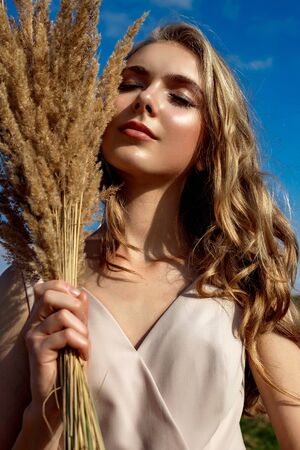 Portrait of a blonde young girl model who stands and poses on a sunny day against a background of haystacks and blue sky enjoying the rays of the sunの写真素材