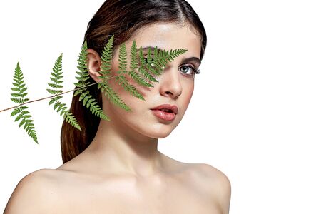 Portrait of an adult brunette woman on a white background with green fern, skin care concept,...