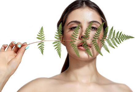 Portrait of an adult brunette woman on a white background with green fern, skin care concept, beautiful skin and hands with nail manicure.の写真素材