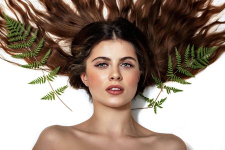 Portrait of an adult brunette woman on a white background with green fern, skin care concept,...
