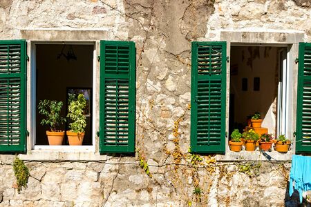Authentic house with a stone wall, with beautiful old open windows and with green shutters, and with vases on the window. Montenegroの写真素材