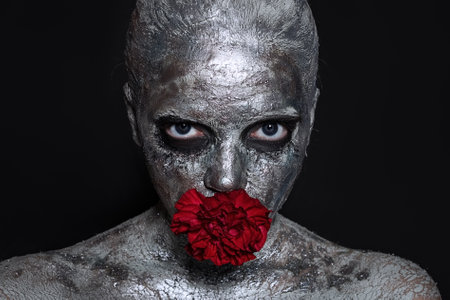 Portrait of a Beautiful young woman with a clay mask on her face, which is covered with silver paint
