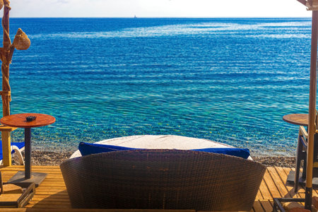 View of the cafe area on the beach. Wooden chairs with tables and deck chairs on the beach at a...