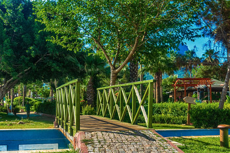 Beautiful summer landscape. View of the path and the bridge in a green garden with green trees along the embankment in Kemer, Turkey. In the background are beautiful mountains and the sea.の写真素材