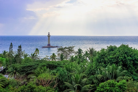 View of a lighthouse in the sea near a rocky shore with palm trees. End of the World Park, Sanya.の写真素材