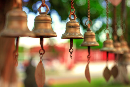 Antique bronze bells hang from chains against a backdrop of greenery and soft bokeh.