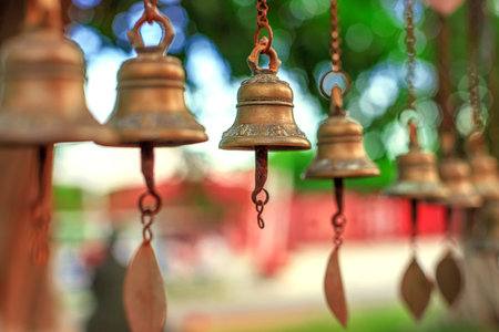 Antique bronze bells hang from chains against a backdrop of greenery and soft bokeh.の写真素材