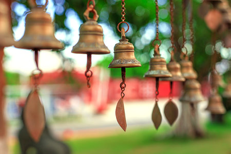 Antique bronze bells hang from chains against a backdrop of greenery and soft bokeh.の写真素材