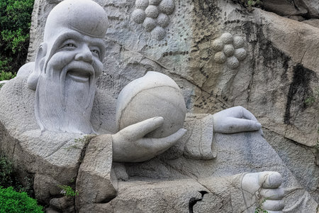 A stone sculpture of a sage against a backdrop of cliffs and greenery at the Heavenly Grottoes Park, Hainan.の写真素材