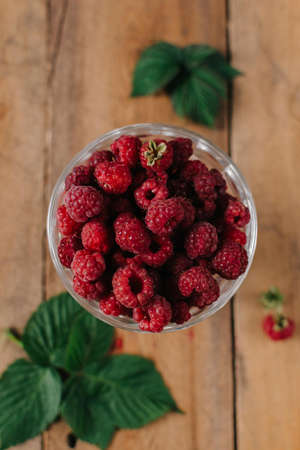 Fresh raspberries in glass vase on wooden background Flatlay