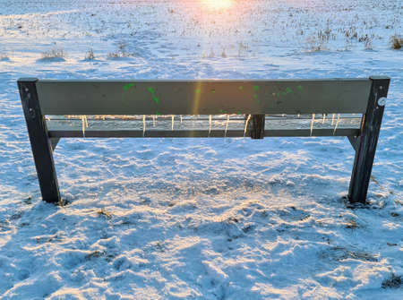 Wooden bench with icicles on it with shining sun on the background