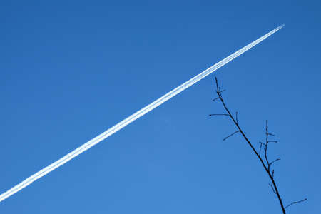 Highly flying plane vapor trail across the blue bright skyの写真素材