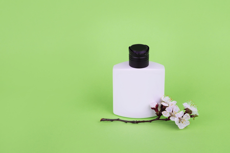 White bottle on a green background. bottle and white flowers. Massage and leaves. Natural cosmetic product. organic green leaves. Essential oil with herbal extract.の写真素材