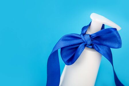 Blue bow and white bottle. Gift for a man. Body cream on a blue background.の写真素材