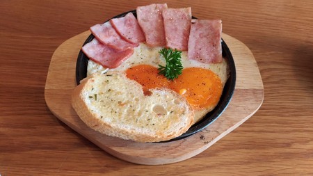 pan-fried egg with topping ham and garlic bread on the hot pan woodの写真素材
