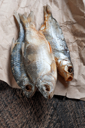 Salty dry river fish is on crumpled yellow paper  on a brown wooden backgroundの写真素材