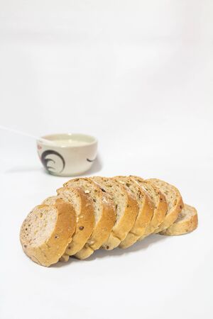 Cereal bread mixed with white sesame seeds, sprinkle with oatmeal, soy milk in a ceramic cup and spoon.の写真素材
