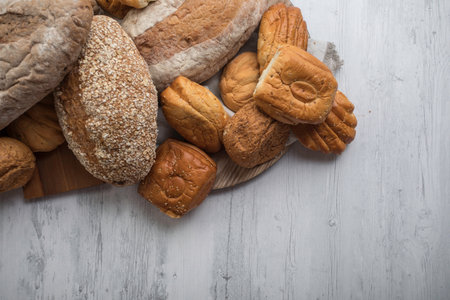 Variety of bread and buns on wooden background. top view. Freshly baked wheat bread loaf breakfast...