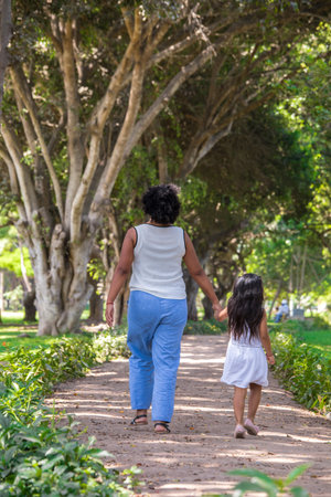 Rear view of mother and daughter holding hands while walking in park
