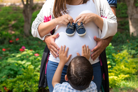 Pregnant woman and her son holding baby shoes in the parkの写真素材