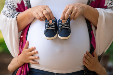 Close up of pregnant woman holding baby shoes in her hands, outdoorの写真素材