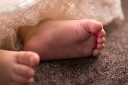 Feet of a newborn baby in a white dress on a brown backgroundの写真素材