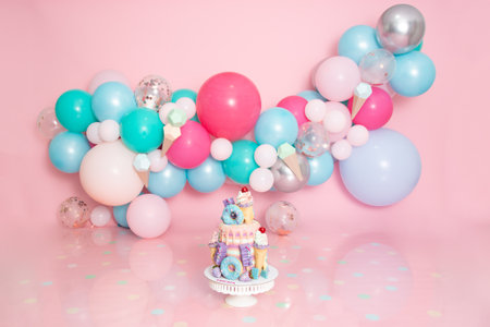 Birthday cake with colorful balloons and confetti on pink background.の写真素材