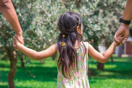 Back view of father and daughter holding hands in olive tree garden.の写真素材