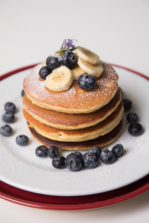 Stack of pancakes with fresh blueberries and banana on a white plateの写真素材