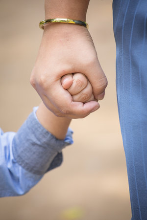 Close up of parent and child holding hands together in the park.