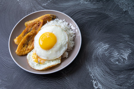 Fried egg with banana and rice on a plate on a dark backgroundの写真素材