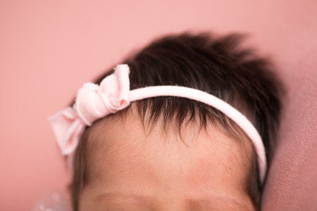 Newborn baby girl with pink bow on her head on pink backgroundの写真素材