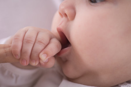 Closeup of a baby's hand in the mouth of his motherの写真素材