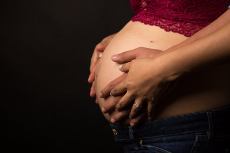Pregnant woman holding her hands on her belly on black backgroundの写真素材