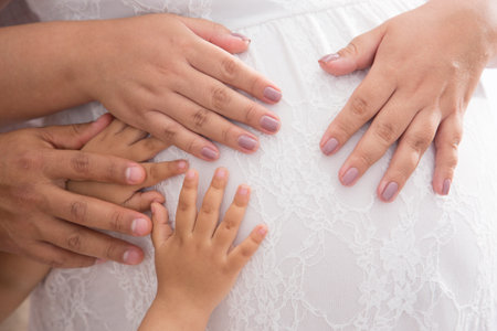 Pregnant woman and her husband holding hands on white background.の写真素材
