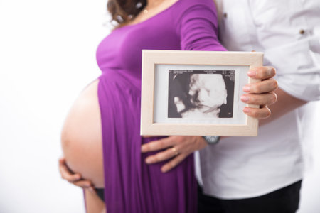 Pregnant woman holding ultrasound scan of her belly in front of white background