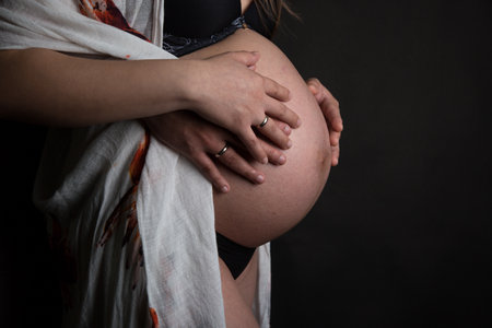 Pregnant woman holding her hands on her belly, black backgroundの写真素材