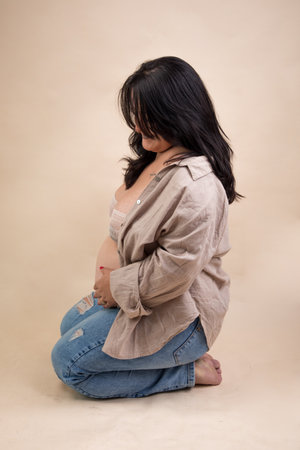 pregnant asian woman sitting on the floor and touching her belly