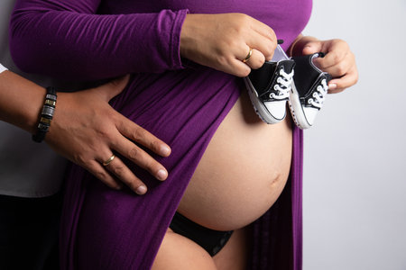 Pregnant woman holding shoes on her belly, close up shot
