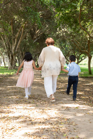 Rear view of mother and children walking in park on a sunny dayの写真素材