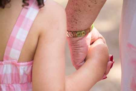 Close-up of mother and daughter holding hands in the park.