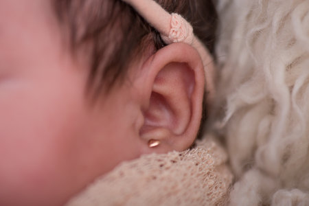 Newborn baby girl with earring closeup. Newborn baby listening to music.