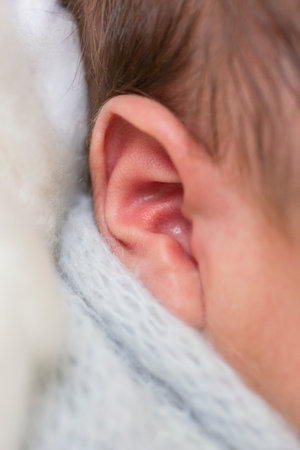 Close-up of a newborn baby's ear in a white scarfの写真素材