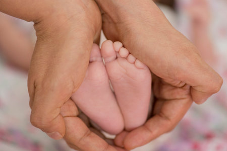 Close-up of newborn baby feet in hands of mother at homeの写真素材