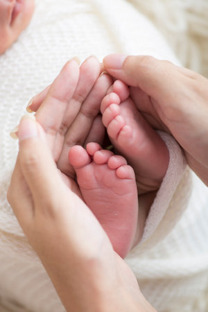 Mother's hands holding the foot of her newborn baby, soft focus background
