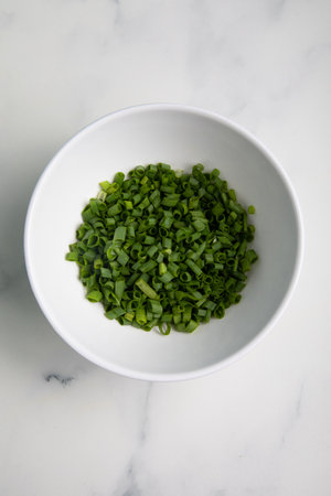 Chopped green onion in a bowl on a white marble table.の写真素材