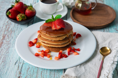 Pancakes with strawberries and honey on a blue wooden background.