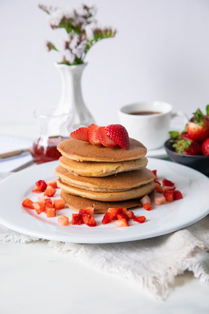 Pancakes with strawberries and honey on a white wooden background.