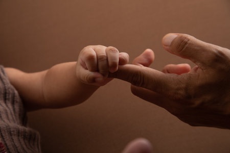 Close-up of a father and son holding hands on brown background